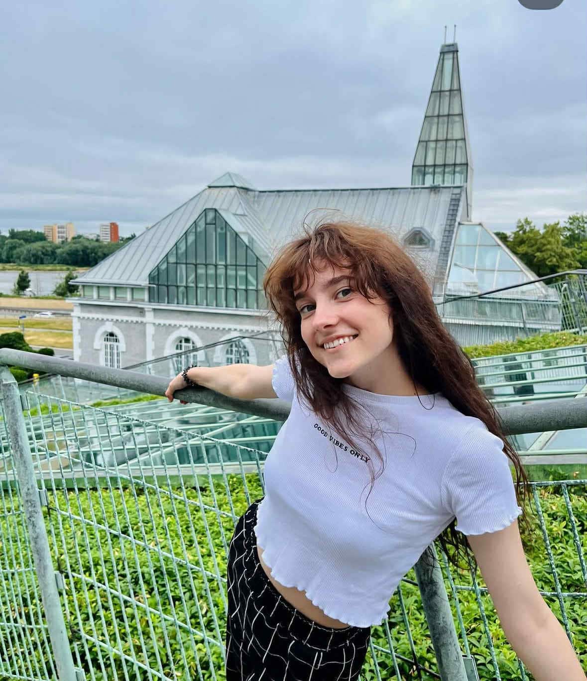 1. Attēls ar sievieti, kas atrodas modernā parks ar stikla arhitektūras būvi fonā, mierīga un radoša atmosfēra, ideāli piemērots blogiem un digitālās mārketinga SEO.